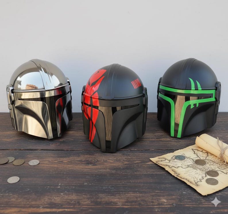 May include: Three Mandalorian helmets in a row. The first is chrome, the second is black with red accents, and the third is black with green accents. A rolled-up map and coins are on the wooden surface.