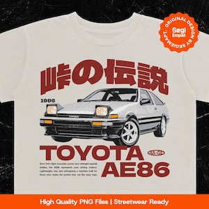 May include: An off-white t-shirt featuring a graphic of a 1986 Toyota AE86 car. The design includes the Japanese text 峠の伝説, the text TOYOTA AE86, and descriptive English text about the vehicle. A circular orange badge reads ORIGINAL DESIGN BY SEGIEMAPT.