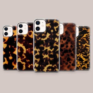 Op de afbeelding: Vijf telefoonhoesjes met een schildpadpatroon in bruin- en geeltinten. De hoesjes hebben een transparante rand en een camera-uitsparing. De hoesjes zijn in een rij gerangschikt, wat de verscheidenheid aan patronen laat zien.