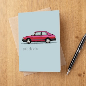 Könnte beinhalten: Eine Grußkarte mit hellblauem Hintergrund zeigt eine rote Autoillustration. Der Text "cult classic" steht unter dem Auto. Ein brauner Umschlag und ein schwarzer Stift mit silbernen Akzenten sind ebenfalls sichtbar.