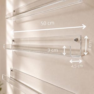 Puede incluir: Tres estantes de pared de acrílico transparente con herrajes de montaje metálicos. Los estantes miden 50 cm de largo, 7 cm de altura total, 3 cm de altura del borde frontal y 4,5 cm de profundidad. El diseño presenta un perfil rectangular.