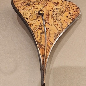 May include: An abstract decorative object with a light brown, patterned surface and a dark metal border. A thin, silver-coloured stem extends from the bottom, with a small, gold-coloured sphere at the top.