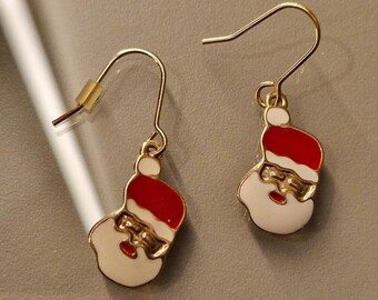 May include: A pair of gold-colored Santa Claus earrings. Each earring features a red hat, white face, and gold-colored details. The earrings have a hook closure.