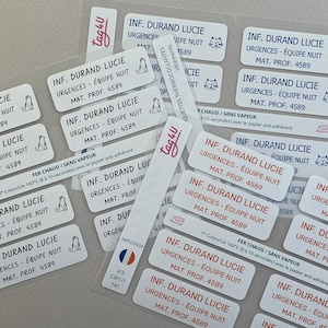 Puede incluir: Un conjunto de etiquetas rectangulares blancas con texto rojo y una ilustración de gato. Las etiquetas dicen "INF. DURAND LUCIE URGENCES - ÉQUIPE NUIT MAT. PROF. 4589". Algunas etiquetas incluyen una bandera francesa.