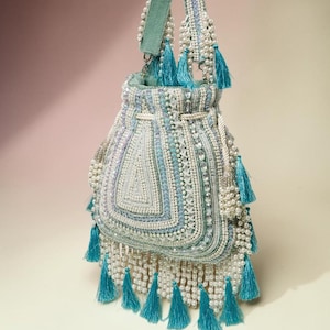 May include: A drawstring handbag in shades of light blue and white, heavily embellished with intricate beadwork, faux pearls, and sequins. The bag features a structured handle, multiple hanging turquoise tassels, and a beaded fringe along the base.