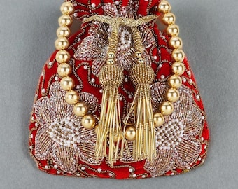 Könnte beinhalten: Ein roter Samtbeutel mit goldenen Perlenakzenten und floraler Stickerei. Die Tasche hat einen Perlenhenkel und zwei goldene Quastenverzierungen. Der Beutel wird wahrscheinlich zum Tragen kleiner Gegenstände verwendet.