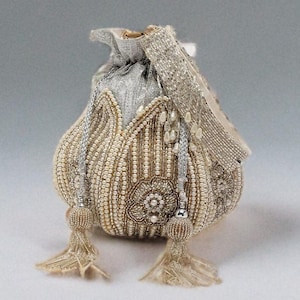 Puede incluir: Pequeño bolso con cordón y cuentas en crema, plata y oro. El bolso presenta intrincados abalorios, un diseño floral y borlas colgantes. El bolso mide aproximadamente 15 cm de alto.