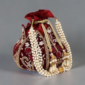 Może przedstawiać: Bordowa aksamitna torebka ze skomplikowanymi złotymi haftami i kwiatowymi wzorami. Torebka ze sznurkiem ozdobiona jest białymi sznurami pereł i złotymi frędzlami, tworząc elegancki i bogaty dodatek.