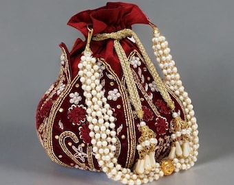 Könnte beinhalten: Ein burgunderfarbener Samtbeutel mit aufwendiger Goldstickerei und floralen Mustern. Der Kordelzugbeutel ist mit weißen Perlenschnüren und goldenen Quasten verziert und schafft ein elegantes und verziertes Accessoire.