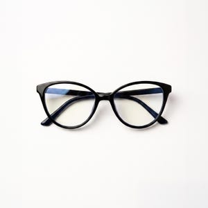 May include: A pair of black-framed eyeglasses featuring a cat-eye silhouette with clear lenses. The frames are constructed with a smooth, glossy finish and include a thin bridge connecting the two rounded, slightly pointed outer edge lenses.