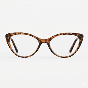 Puede incluir: Gafas de ojo de gato con un patrón de carey. Las monturas son marrones con detalles negros y las lentes son transparentes. Las gafas están sobre un fondo blanco liso.