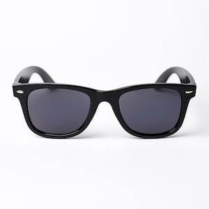 Könnte beinhalten: Schwarze Sonnenbrille mit dunklen Gläsern. Die Sonnenbrille hat ein klassisches, rechteckiges Rahmendesign. Die Bügel der Sonnenbrille sind leicht gebogen. Die Sonnenbrille ist vor einem weißen Hintergrund platziert.