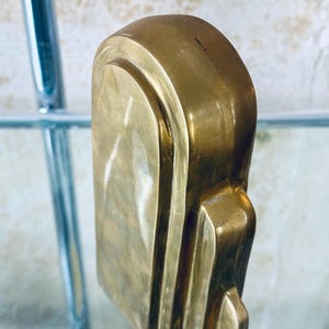 May include: A close-up of a solid brass art deco style door handle. The handle has a rectangular shape with rounded edges and vertical grooves. The brass has a polished finish, reflecting light.