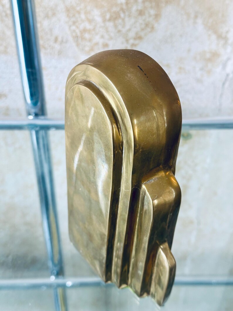 May include: A close-up of a solid brass art deco style door handle. The handle has a rectangular shape with rounded edges and vertical grooves. The brass has a polished finish, reflecting light.