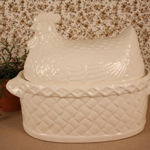 May include: A white ceramic hen-shaped covered dish. The lid is a detailed hen, and the base is a basket weave design. The dish is a decorative kitchen item.