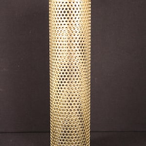 May include: A cylindrical, gold-colored metal lampshade with a perforated design. The lampshade is tall and narrow, with a consistent pattern of small, evenly spaced holes throughout its surface. The object is likely used for home decor.