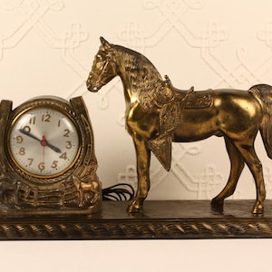 May include: A vintage brass-toned clock featuring a horse figurine. The clock has a round face with black numerals and red hands. The horse is saddled and stands on a rectangular base. The clock is a decorative item.