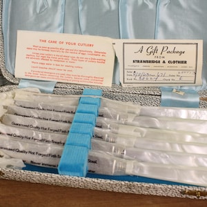 May include: A vintage cutlery set in a blue and white patterned case. The set includes multiple knives, each individually wrapped. The case contains a card with care instructions and a gift package label from Strawbridge & Clothier.