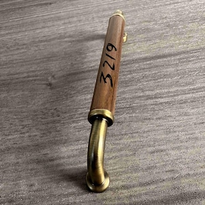 May include: A cylindrical cabinet handle featuring a dark brown wood centre section and brushed brass metal ends. The wood portion is marked with the black handwritten text 3219. The handle has a curved mounting post at the visible end.
