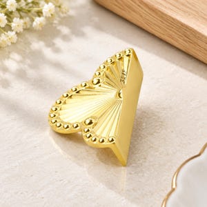 May include: A gold-colored metal cabinet knob shaped like a fan with a textured, radiating sunburst pattern and a border of small, raised circular beads. The surface features the engraved text 321Y near the top edge of the fan-shaped design.