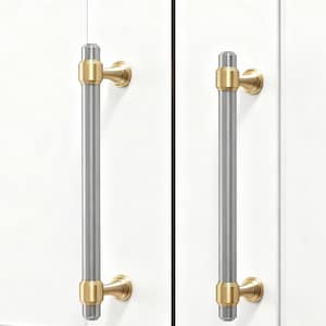 May include: Two cabinet pulls with a brushed silver center and gold-toned accents. The pulls are cylindrical with gold rings at each end and a gold base. They are mounted on a white cabinet door.