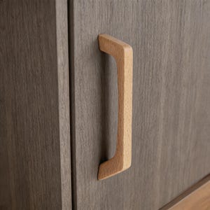 Könnte beinhalten: Nahaufnahme einer Holzschranktür mit einem hellfarbigen, gebogenen Holzgriff. Die Schranktür ist dunkelgrau mit einer Holzmaserung. Der Griff hat eine helle, natürliche Holzfarbe.