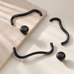 May include: Two matte black curved cabinet pulls and two matching round cabinet knobs. Each piece features the engraved number 3219 in a stylised font. The hardware has a smooth finish and a consistent dark colour throughout the set.