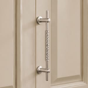 May include: A brushed nickel cabinet pull with a textured center section and a T-shaped design. The hardware is mounted on a light beige cabinet door. The pull is designed for easy gripping and adds a modern touch to any kitchen or bathroom.