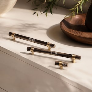 May include: Two long cylindrical dark wood cabinet pulls and one small matching knob, each featuring brushed gold metal accents and the engraved white text 3219. The hardware pieces are arranged in a staggered formation on a flat surface.