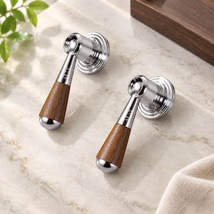 May include: Two faucet handles featuring a polished chrome finish and a dark brown wood grain grip. Each handle has a circular base with concentric rings and a tapered lever design. The word ALAS is engraved on the chrome neck of each handle.