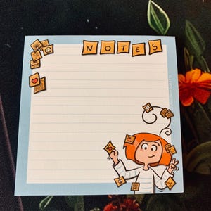 Peut inclure: Un bloc-notes bleu clair avec le mot "NOTES" en haut. Une illustration de dessin animé d'une personne aux cheveux roux tient des notes. Le bloc-notes a du papier ligné et de petits post-it avec diverses icônes.