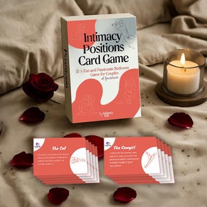 May include: A card game box and cards with the title "Intimacy Positions Card Game". The box has a white and coral design, with the text "A Fun and Passionate Bedroom Game for Couples of hoursbede". A lit candle and rose petals are also visible.