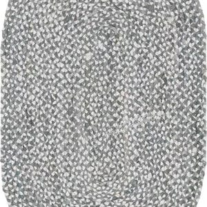 Puede incluir: Una alfombra trenzada de forma ovalada que presenta un patrón texturizado de fibras entrelazadas en gris y blanco. La alfombra muestra un tejido denso y consistente en toda su superficie, creando un aspecto moteado con un esquema de color uniforme.
