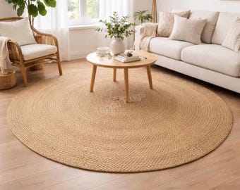 May include: A large, round, natural-colored jute area rug with a braided texture. The rug features a circular weave pattern and is placed on a light-toned wooden floor. The surface of the rug displays a visible watermark text that reads Happy Rugs.