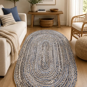 May include: Oval braided rug in natural and blue tones. The rug features a concentric design with alternating bands of natural jute and blue fibers. This floor covering adds a touch of rustic charm to any living space.