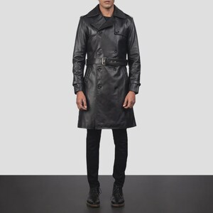 Könnte beinhalten: Ein schwarzer Ledertrenchcoat mit doppelreihigem Design, Gürtel und klassischem Kragen. Der Mantel ist knielang und hat ein elegantes Aussehen. Das Model trägt eine schwarze Hose und Schuhe.