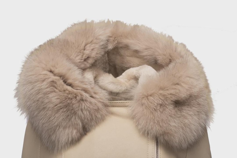 Puede incluir: Primer plano de una chaqueta beige con un gran cuello de piel suave de color marr&oacute;n claro. La chaqueta tiene una cremallera y una textura suave similar al cuero. El cuello de piel a&ntilde;ade un elemento lujoso y c&aacute;lido.