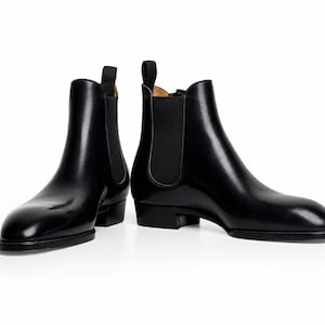 May include: A pair of black leather Chelsea boots featuring a smooth, polished finish, rounded toes, low stacked heels, and black elastic side panels with vertical pull tabs at the top of the ankle collars for a sleek, streamlined appearance.