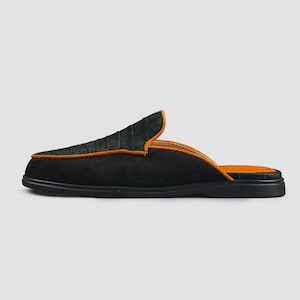 Pode incluir: Chinelo de camurça preto com vamp texturizado cinza escuro e acabamento laranja. O design de costas abertas apresenta uma sola preta e um interior laranja contrastante. Uma opção de calçado elegante e confortável.
