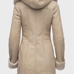 Puede incluir: Un abrigo largo de invierno color crema con capucha y pu&ntilde;os forrados de piel. El abrigo presenta un dise&ntilde;o a medida con costuras verticales y cierre de botones. El ribete de piel es de color beige claro y el abrigo parece ser de cuero.