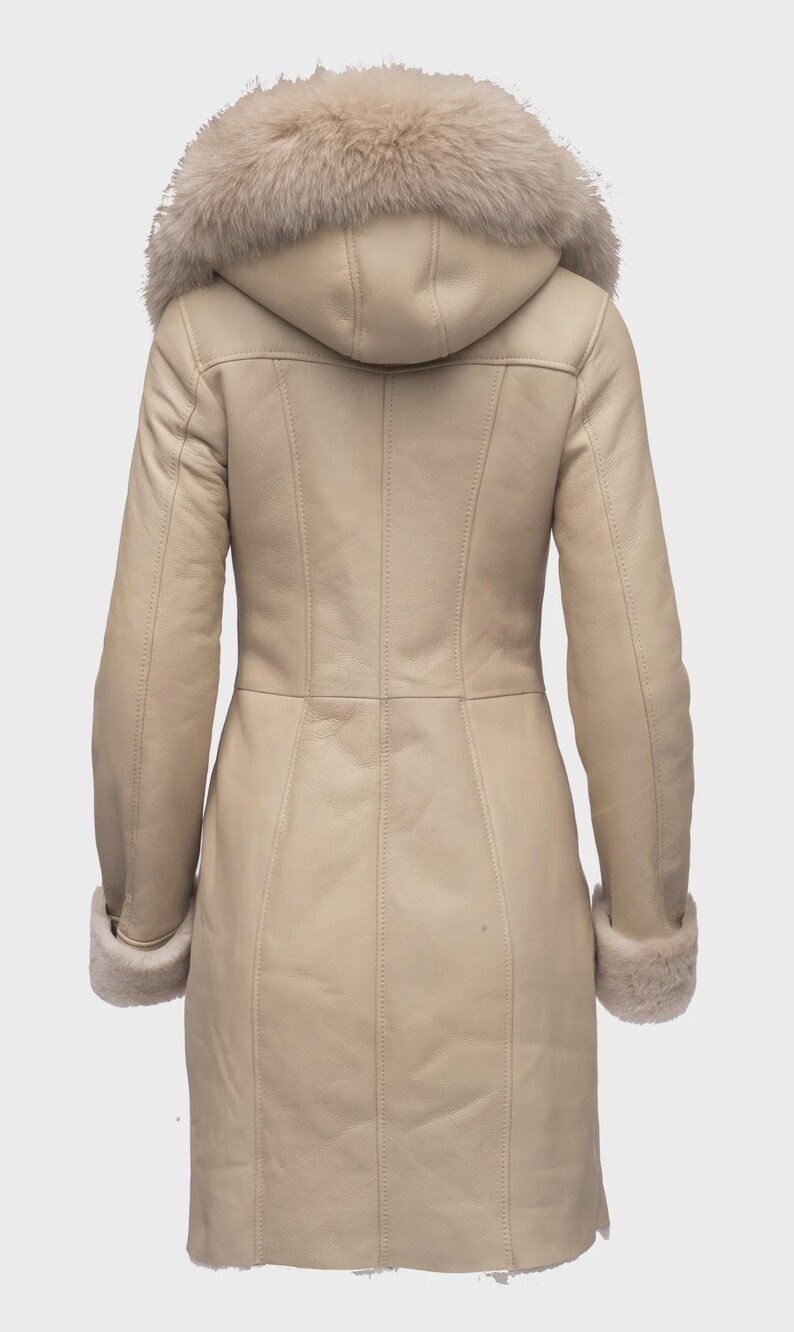 Puede incluir: Un abrigo largo de invierno color crema con capucha y pu&ntilde;os forrados de piel. El abrigo presenta un dise&ntilde;o a medida con costuras verticales y cierre de botones. El ribete de piel es de color beige claro y el abrigo parece ser de cuero.
