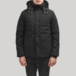 Könnte beinhalten: Schwarze Winterjacke mit Kapuze. Die Jacke hat ein gestepptes Design und einen Frontreißverschluss. Die Kapuze hat Druckknöpfe. Die Person trägt eine schwarze Hose und ein schwarzes Oberteil.