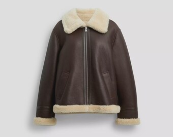 May include: A dark brown jacket with a smooth exterior finish, featuring a thick cream-colored shearling collar, cuffs, and hem. The jacket includes a full-length silver-toned metal zipper closure down the center and two vertical side pockets.