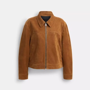 Könnte beinhalten: Eine hellbraune Wildlederjacke mit klassischem Kragen, durchgehendem Metallreißverschluss, langen Ärmeln mit geknöpften Manschetten und zwei Seitentaschen. Das Kleidungsstück hat eine strukturierte Passform mit horizontalen Nähten im Brustbereich.