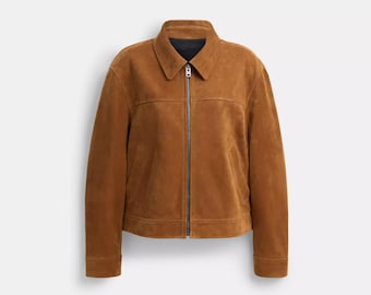 May include: A tan suede jacket featuring a classic collar, a full-length metal front zipper, long sleeves with buttoned cuffs, and two side pockets. The garment has a structured fit with horizontal seam detailing across the chest area.