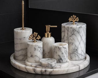 May include: A marble bathroom set with gold accents. The set includes a soap dispenser, toothbrush holder, tumbler, and a lidded jar, all resting on a matching tray. Each piece is adorned with a gold tree-shaped embellishment.