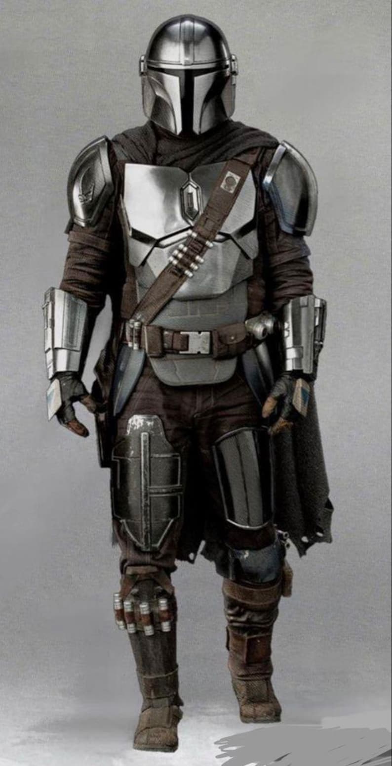 May include: A full-length image of a Mandalorian warrior in silver and dark armour. The helmet is polished silver, and the chest plate is a mix of silver and grey. The warrior wears a brown belt with ammunition pouches and a dark cape.