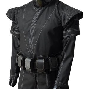May include: Black costume with white stitching details. The outfit features padded shoulder accents and a belt with multiple pouches. The long-sleeved garment has a high neckline and is made of a matte fabric.