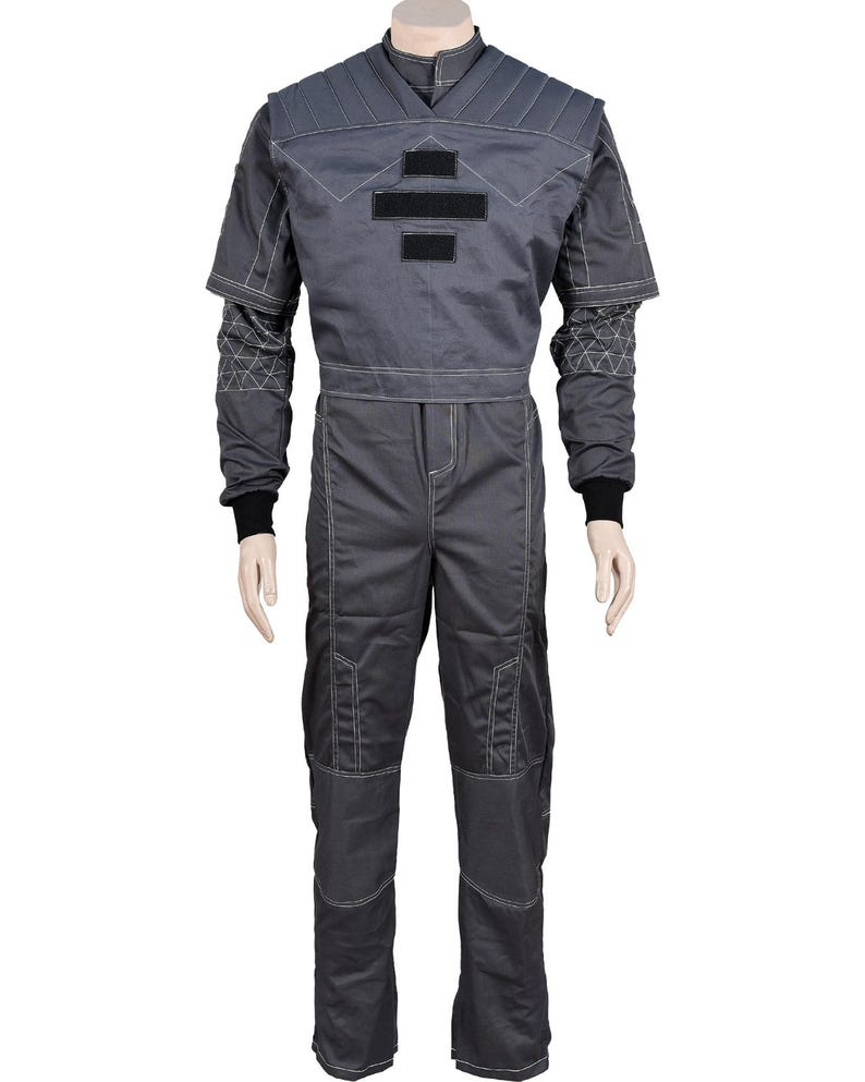 May include: A gray jumpsuit with a quilted upper section and contrasting white stitching. The suit features black accents and a high collar. The sleeves have a geometric pattern near the wrists, and the pants have reinforced knee patches. The overall design suggests a futuristic or tactical aesthetic.