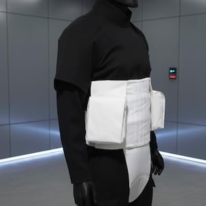 May include: A person in a black costume with a helmet and white accents. The costume includes a black helmet, a long-sleeved top, pants, and a white chest and waist piece. The background is a modern, gray interior.